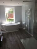 A bathtub by an open window, with a toilet on the left, and a towel drying rack on the right.