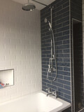 An installed, bath and shower unit with multiple shower heads, and grey tiles behind the unit.