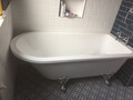 An installed bathtub unit with a shower unit and white tiles behind it.