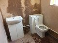 Showing a newly installed toilet and basin combination against a wall with plastering completed, but no wallpapering.