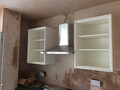 An empty shell of a kitchen cupboard unit on a wall above a hob, with an oven extractor unit between them.
