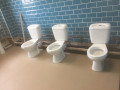 A row of three toilets in a public bathroom, each plumbed in but lacking cubicles.