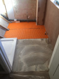 A bathroom floor without any tiles on it, there is tiling cement placed and orange insulating material on the floor ready for the tiles.
