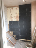 A bathroom wall with a number of missing tiles, ready for more tiles to be installed. The current tiles are black in colour.