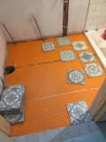 A bathroom floor with orange insulating material installed and a number of tiles, ready to be installed.